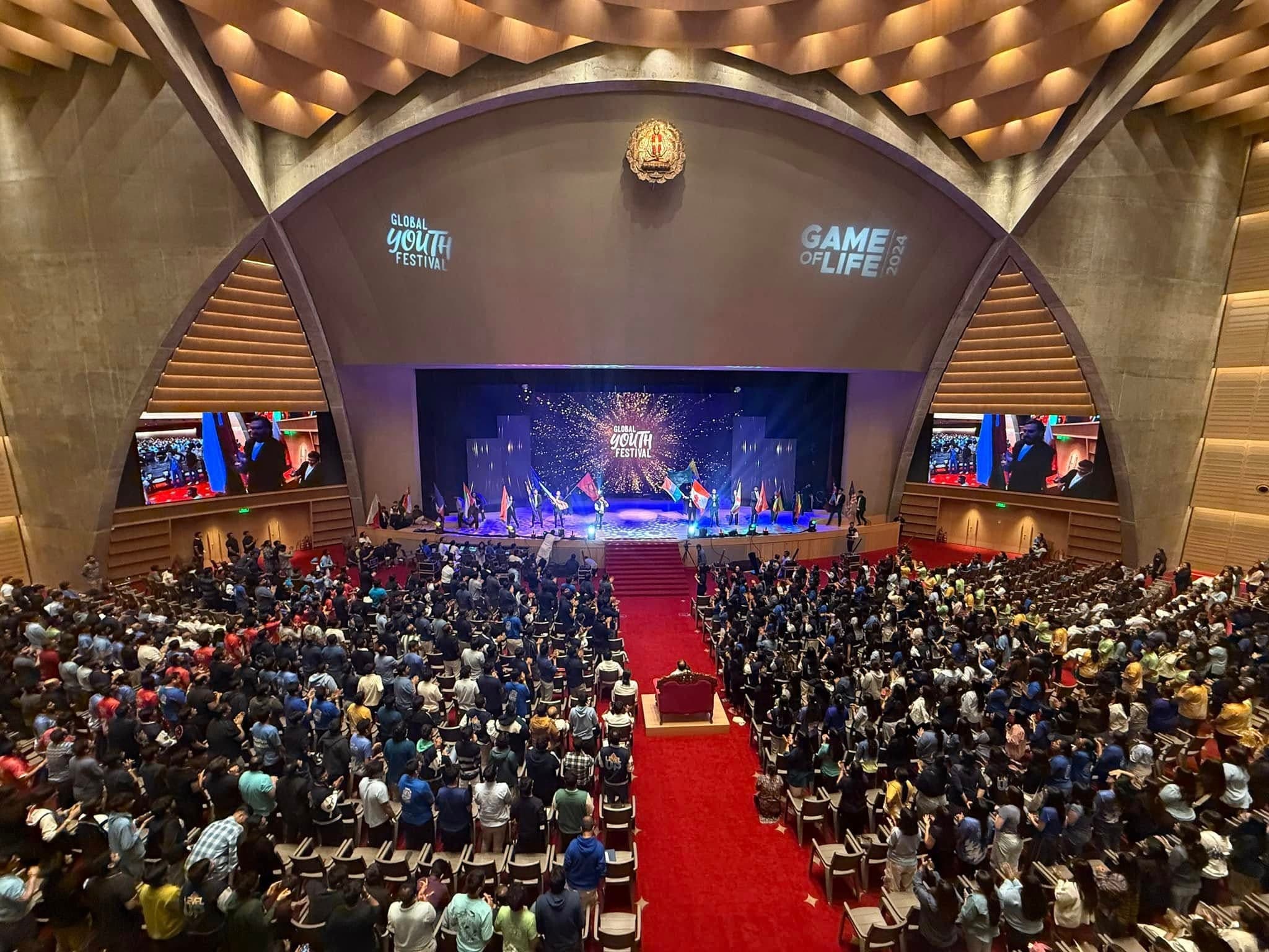 The audience and flag procession fill Dharampur Ashram's auditorium at the 2024 festival