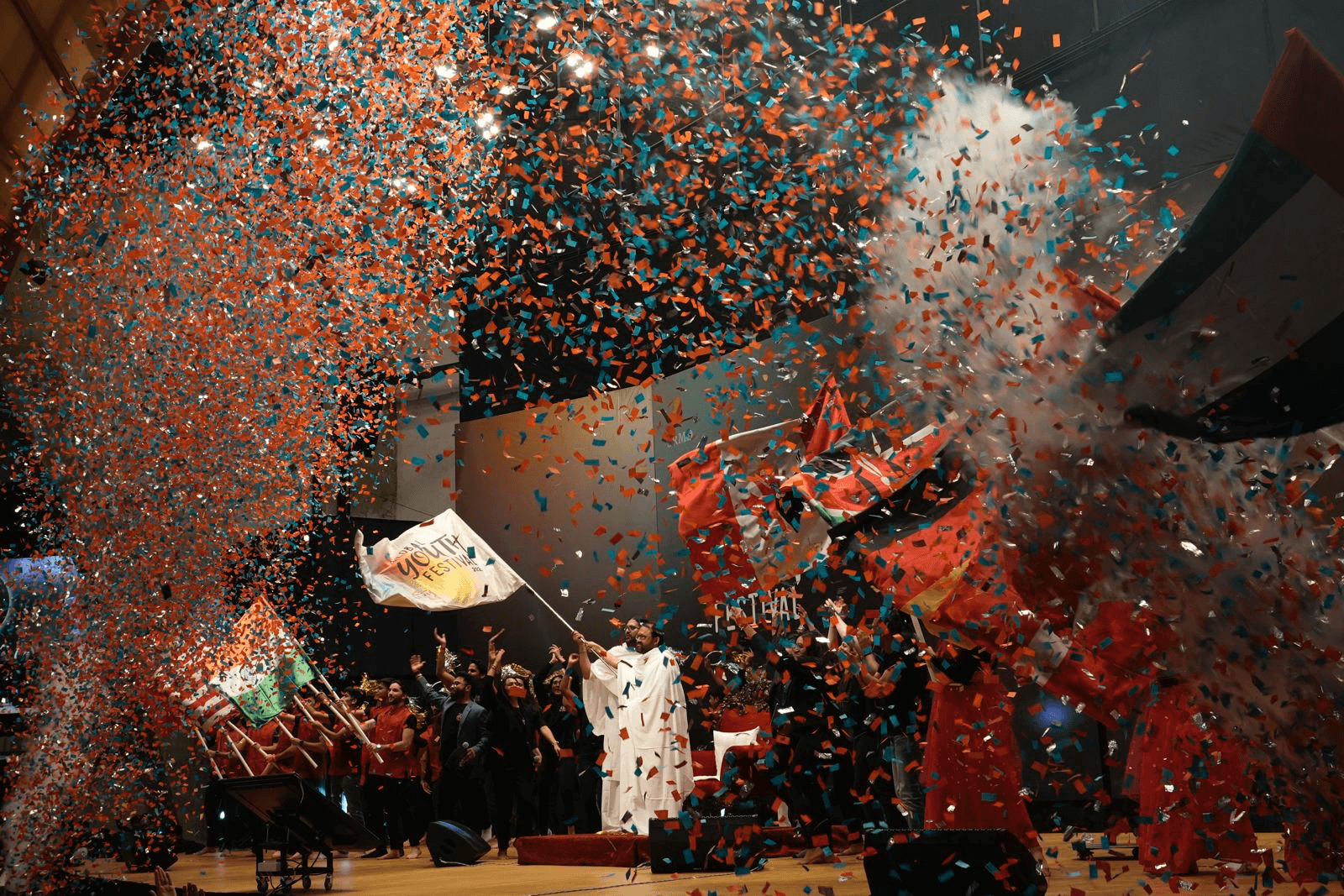 The Global Youth Festival flag is raised on stage amid orange and blue confetti